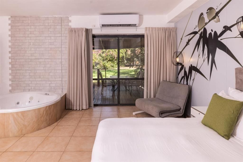 Un dormitorio moderno con una cama grande, una bañera y vistas a un jardín a través de una puerta corrediza de cristal.