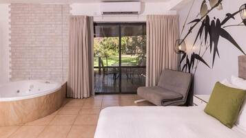 Un dormitorio moderno con una cama grande, una bañera y vistas a un jardín a través de una puerta corrediza de cristal.