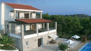 A two-story building with a stone facade, a red-tiled roof, and a balcony with outdoor furniture. - Holiday Home Kaic (Solta)