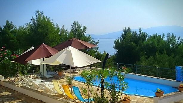 A poolside area with umbrellas, lounge chairs, and a view of the sea. - Holiday Home Kaic (Solta)