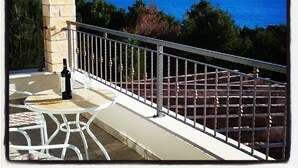A balcony with a stone pillar, a table with chairs, hanging flower pots, and a view of the sea and mountains. - Holiday Home Kaic (Solta)
