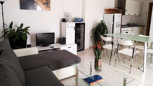 A modern living room with a sofa, TV, and a glass table. There's a kitchen area with cabinets and a refrigerator. - Holiday Home Kaic (Solta)