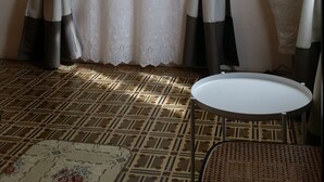A room with patterned flooring, a round table, a wicker chair, and curtains tied back to reveal a window. - Villa Armonia (Lucca)