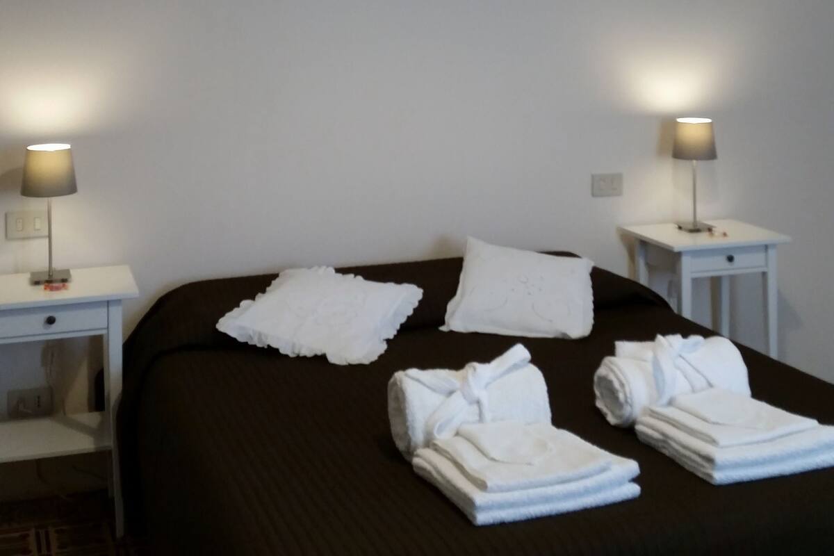 A hotel room with a large bed, two bedside tables with lamps, and neatly folded towels on the bed.