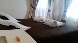 A hotel room with a brown quilted bedspread, white towels, and a white table with a small item on it. - Villa Armonia (Lucca)