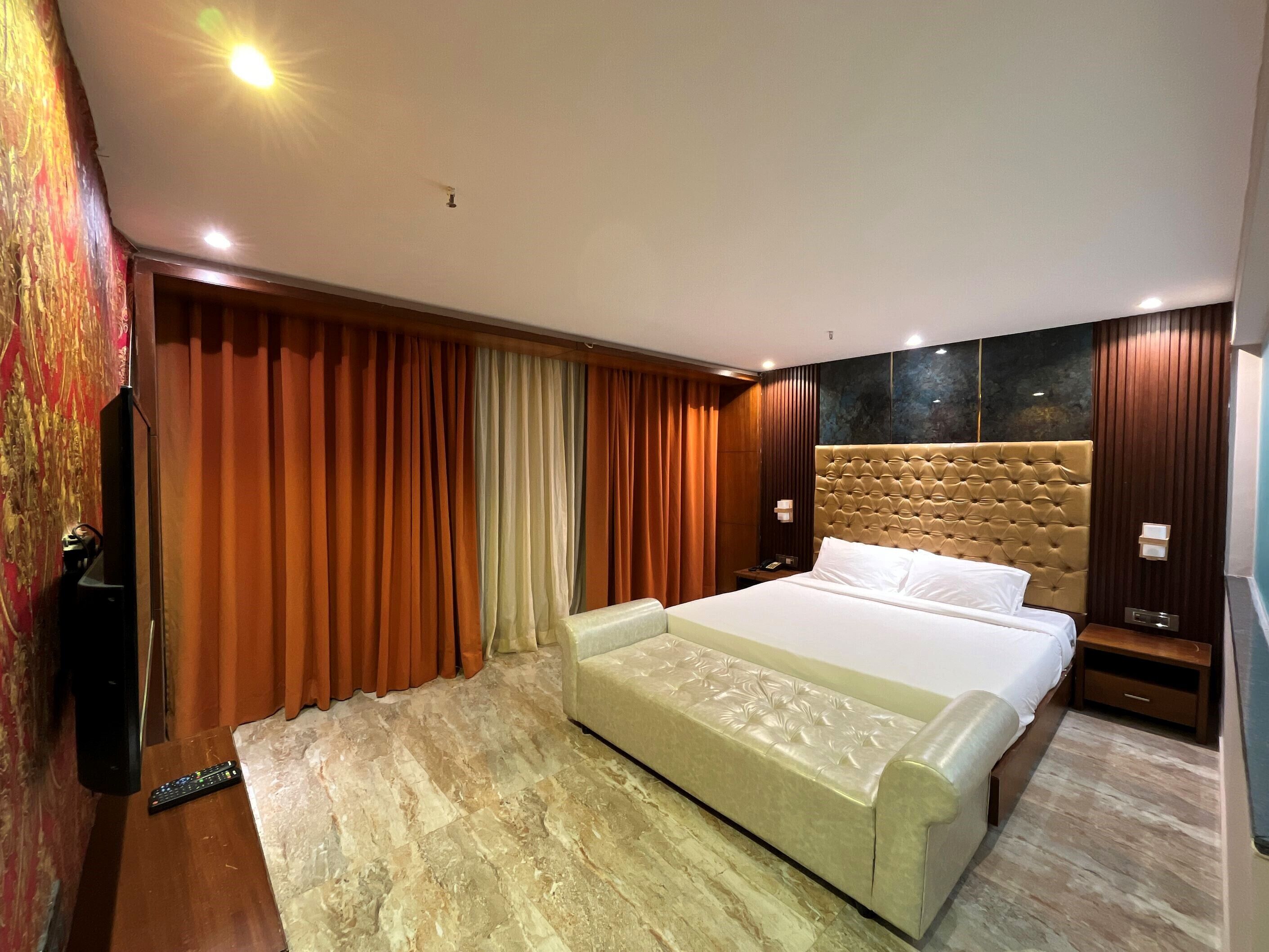 A modern hotel room with a large bed, a flat-screen TV, and a wooden floor.