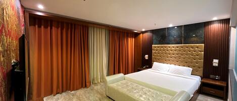 A modern hotel room with a large bed, a flat-screen TV, and a wooden floor.