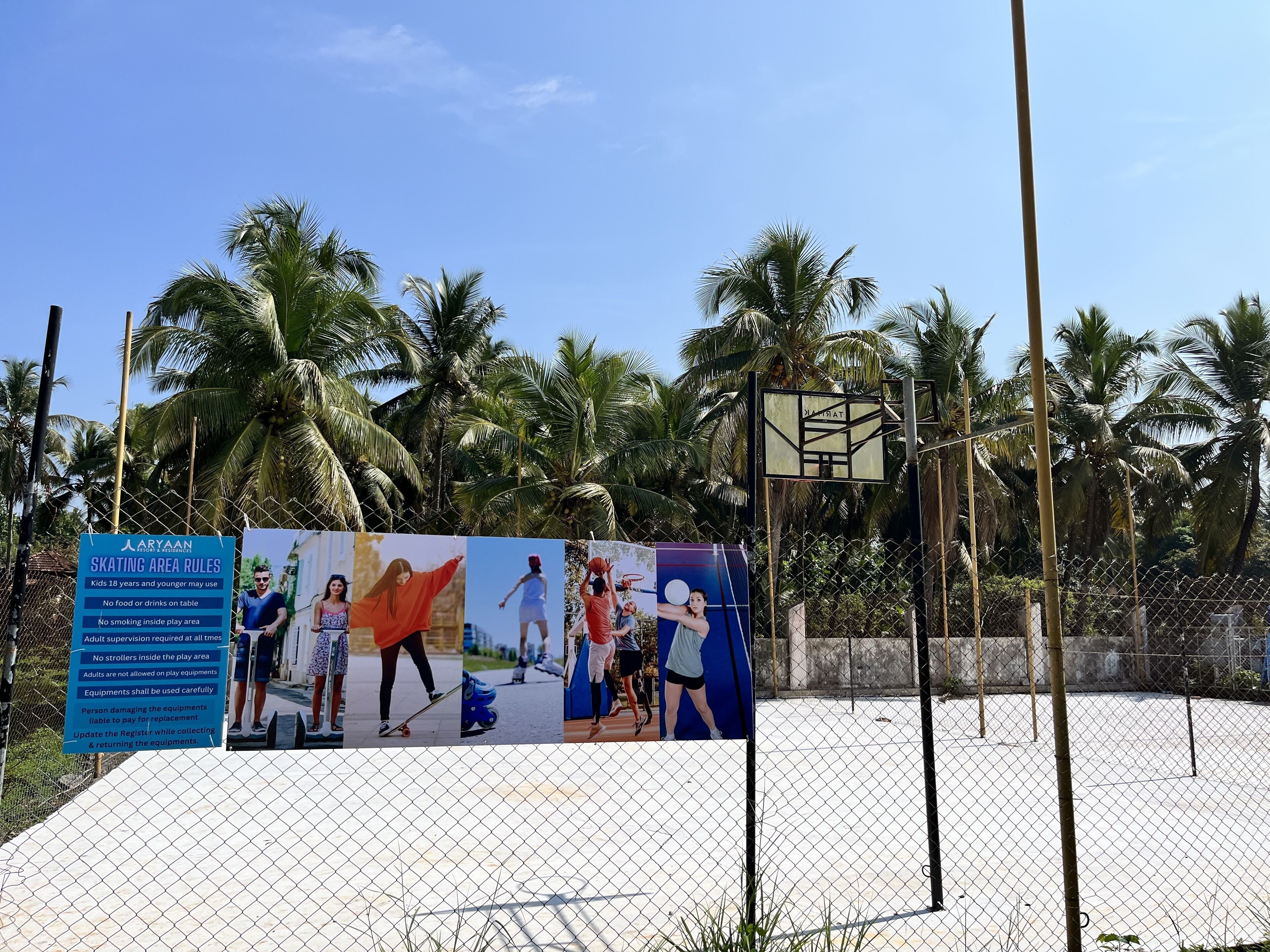 A fenced skating area with a sign detailing rules and a basketball hoop.