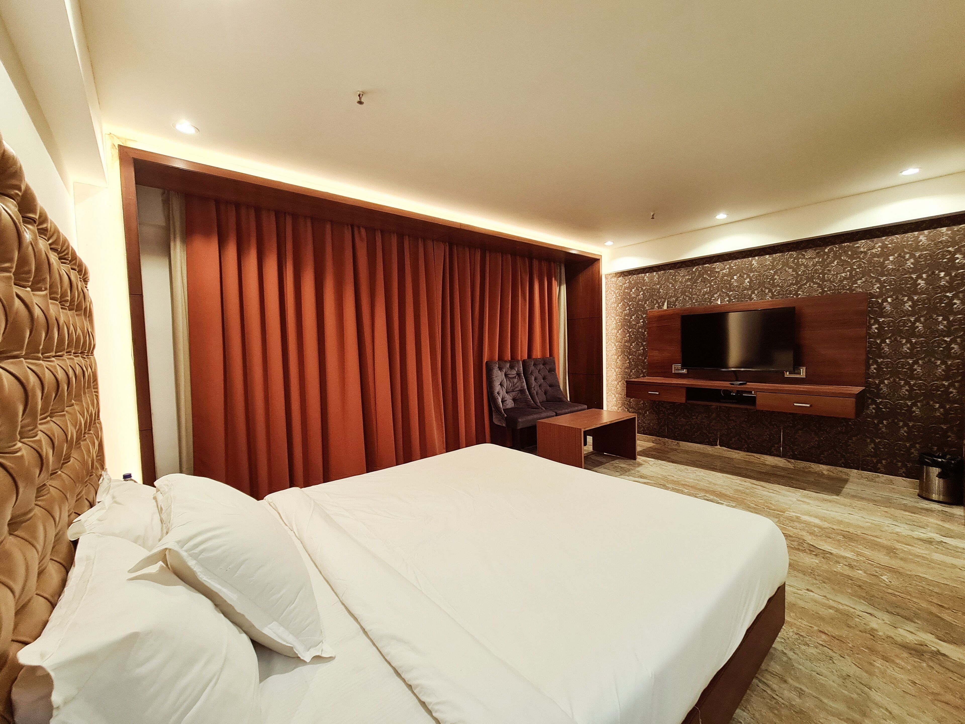 A hotel room with a large bed, a TV mounted on the wall, and a wooden headboard.