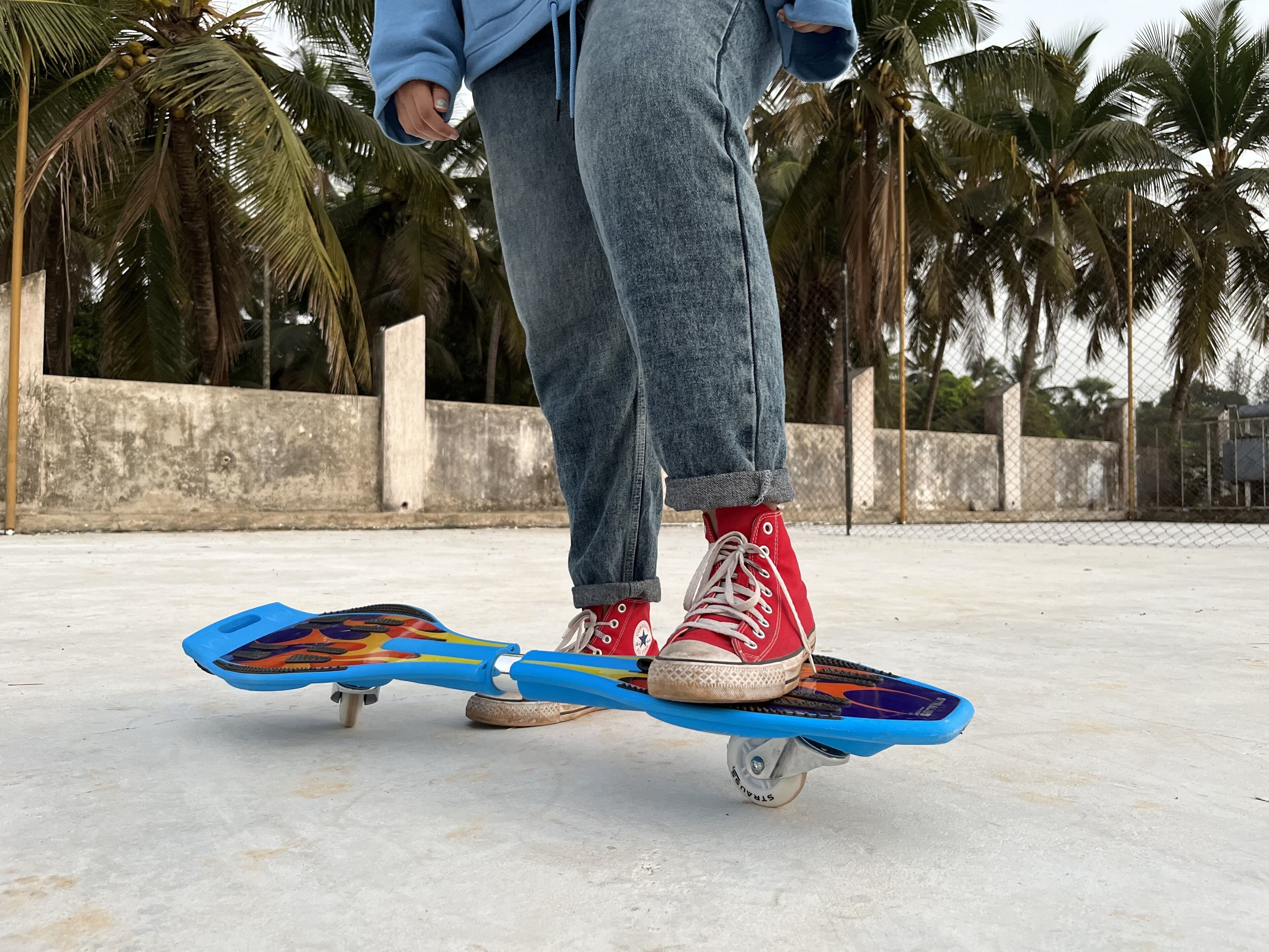 A person standing on a skateboard with a concrete surface and palm trees in the background.