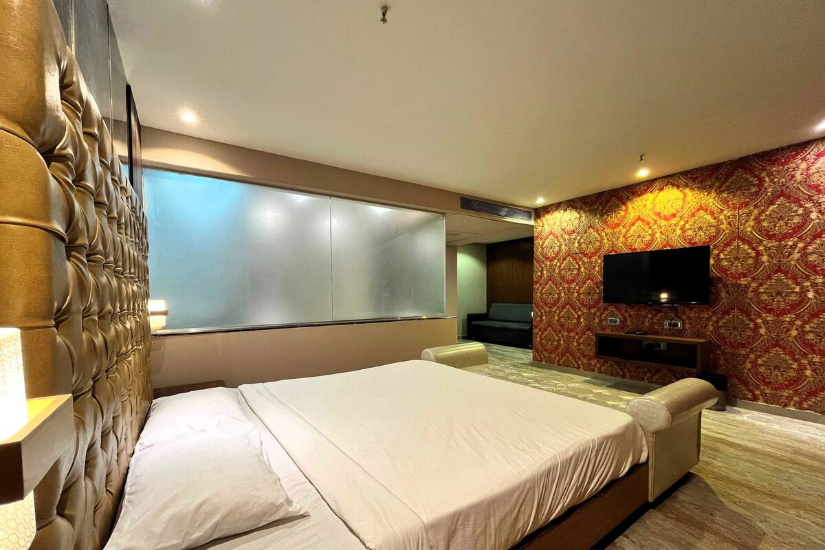 A hotel room with a large bed, a flat-screen TV mounted on the wall, and a patterned wallpaper.