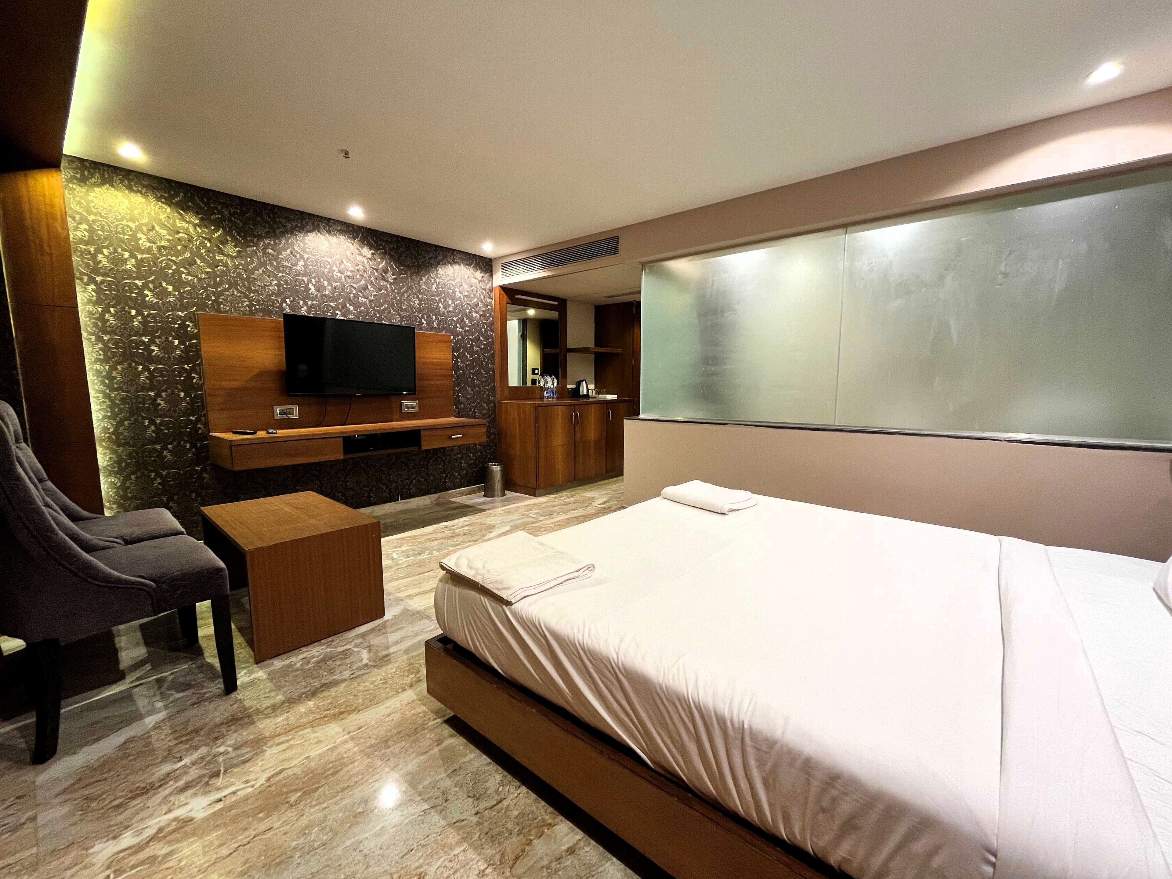 A modern hotel room with a large bed, a TV mounted on a wooden panel, a desk, and a chair.