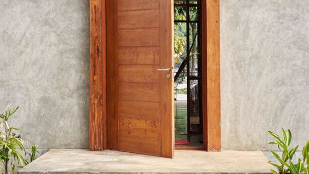 Un bâtiment moderne doté d’une grande porte en bois, d’un escalier en béton et offrant une vue sur l’intérieur à travers la porte.