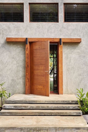 Un edificio moderno con una puerta de madera grande, escalones de concreto y vista al interior a través de la puerta.
