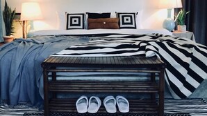 Une chambre à coucher avec un lit, deux lampes de chevet, une table de chevet avec des chaussures et une couverture à rayures.