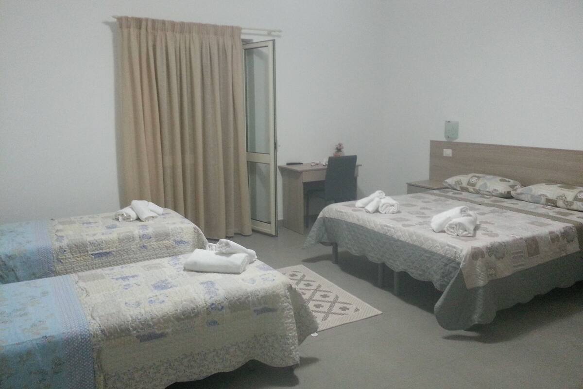 A hotel room with two beds, a desk, a chair, and a window with curtains.