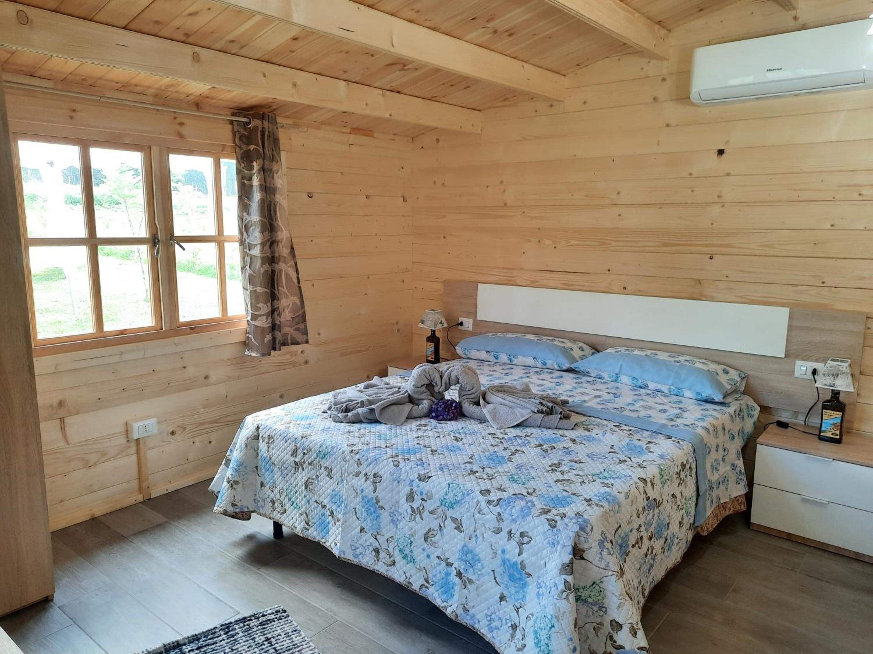 A wooden room with a bed, a nightstand, a lamp, and a window with curtains.