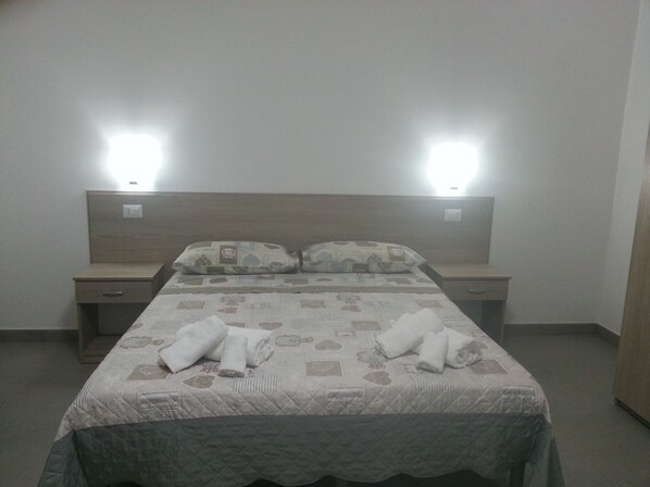 A neatly made bed with a quilted bedspread and two pillows, flanked by bedside tables with lamps.