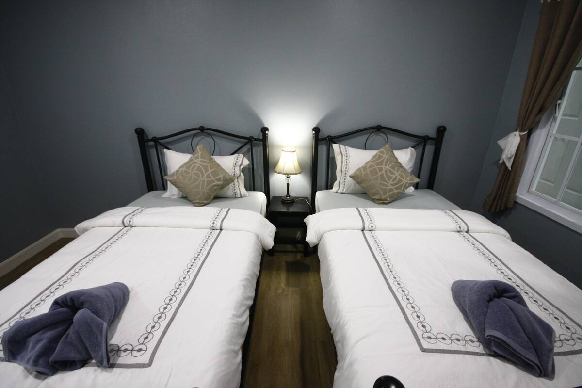 A twin room with two beds, a nightstand, a lamp, and a window with curtains.
