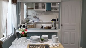 A kitchen with white cabinets, a coffee machine, and a sink. There are plates, glasses, and utensils on the counter. - Sky Cottage (Rayong)