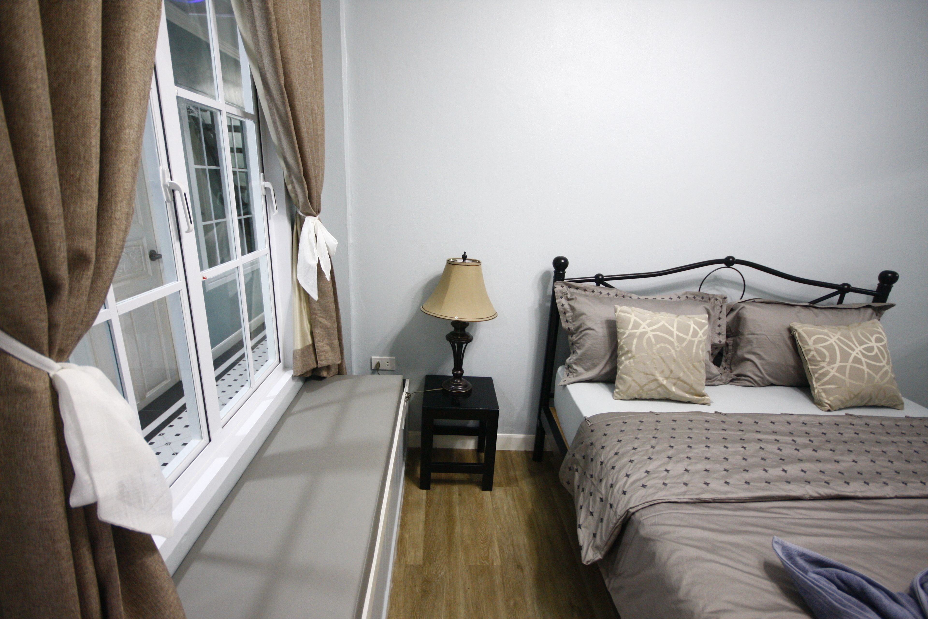 Un dormitorio con cama, una mesita de noche con lámpara, una ventana con cortinas y vistas al exterior.