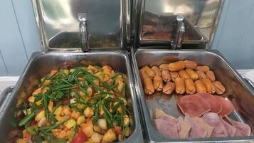 Un bufé con dos secciones: una con guiso de verduras y pollo, y otra con salchichas y embutidos.