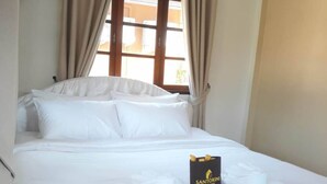 A neatly made bed with white linens, a black Santorini sign, and beige curtains. - Santorini Khanom (Khanom)