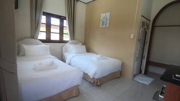 A hotel room with two single beds, a window with curtains, a small painting on the wall, and a door with a floral curtain.