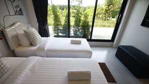 A hotel room with two beds, a sofa, and a large window offering a view of greenery. - Wannachart Boutique Resort (Tha Sala)