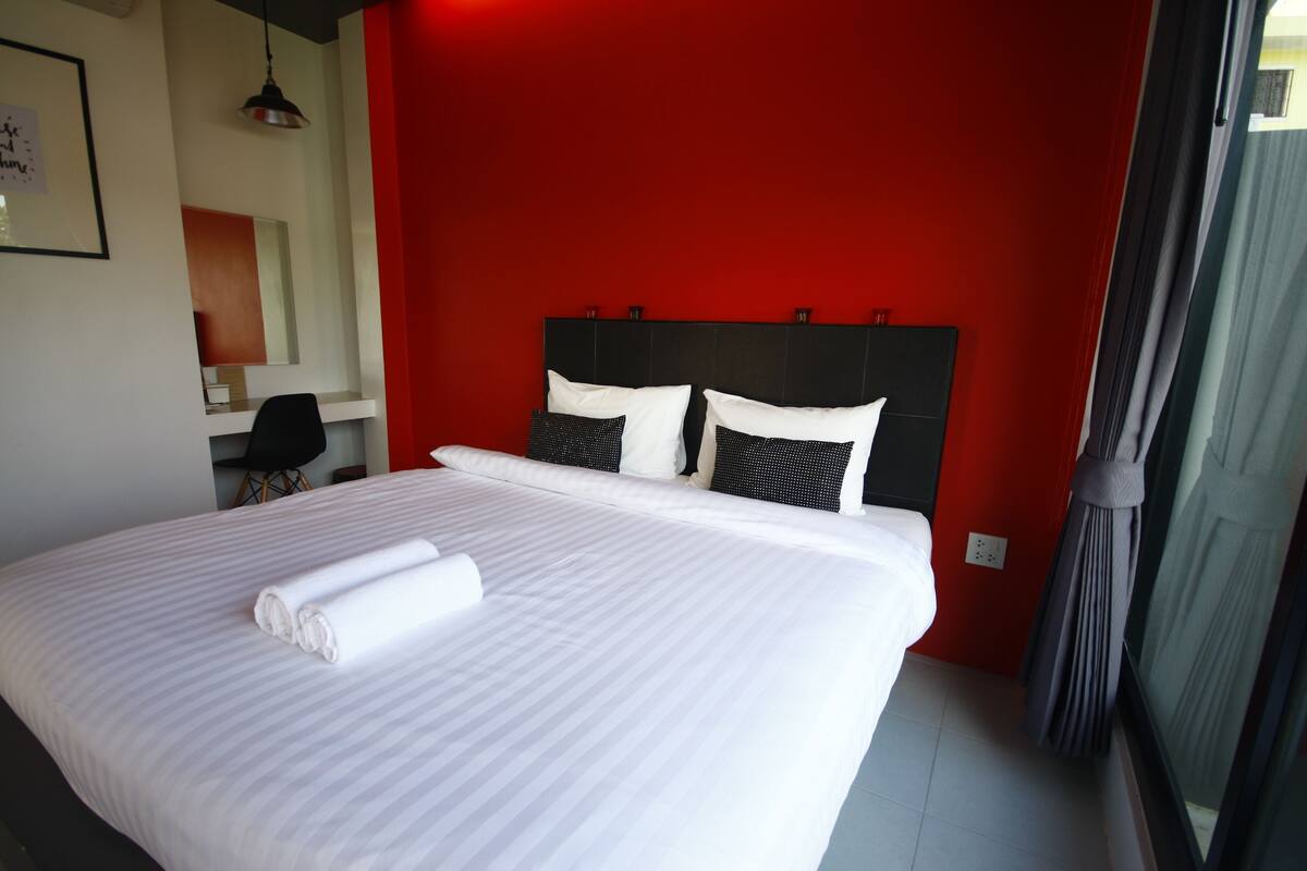 Una cama bien tendida con sábanas blancas y dos almohadas, cabecera negra y pared de acento roja.