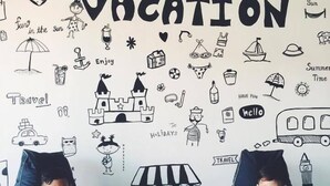Two children sitting on bean bags in a room with a wall decorated with summer vacation-themed drawings and text. - Wannachart Boutique Resort (Tha Sala)