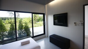 A modern bedroom with a large window, a bed, a bench, and a flat-screen TV mounted on the wall. - Wannachart Boutique Resort (Tha Sala)