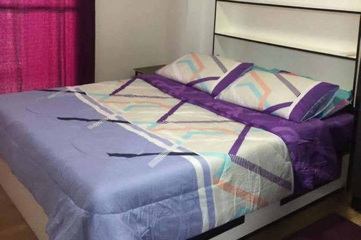 A single-bed room with a headboard, a bed with a patterned bedspread, a purple curtain, and a wall-mounted air conditioning unit.