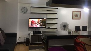 Un salon moderne avec un téléviseur à écran plat, une horloge, un ventilateur et un tableau encadré accroché au mur.