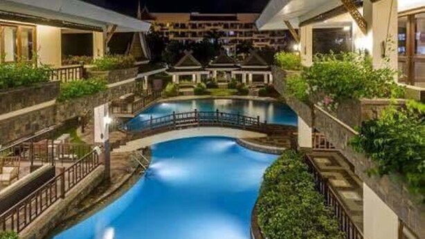Une piscine surmontée d’un pont, entourée d’une végétation luxuriante et de murs en pierre.
