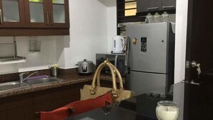 Une cuisine avec des meubles de couleur sombre, un plan de travail noir, un évier en acier inoxydable et un réfrigérateur.