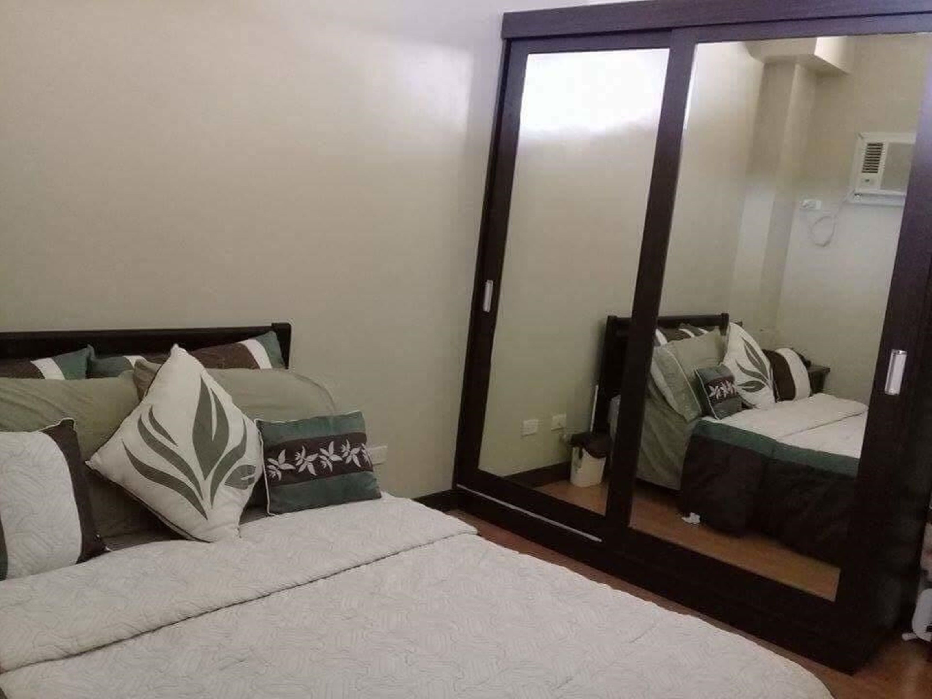 A bedroom with a bed, pillows, a mirror, and a wardrobe.