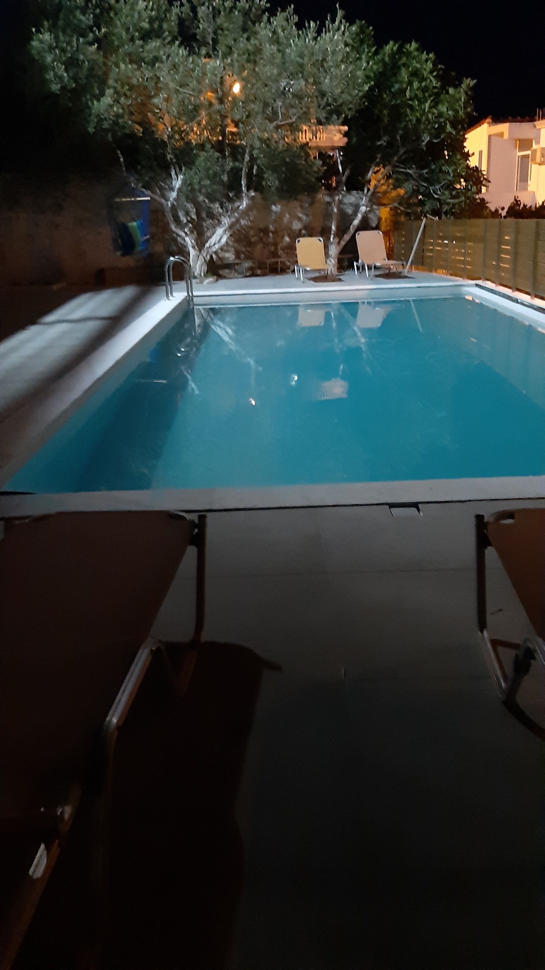 A swimming pool with a clear water surface, surrounded by a low wall and a few lounge chairs.