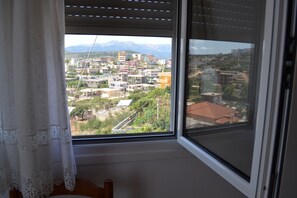 Una habitación con ventana que da a una zona residencial con edificios y montañas a lo lejos.