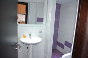 Un baño con un lavamanos blanco, un estante de vidrio y azulejos morados.