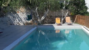 Une piscine avec deux chaises longues et un mur de pierre en arrière-plan.