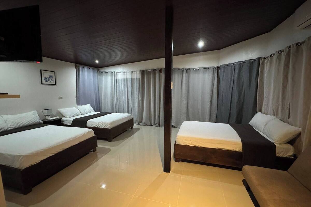 A hotel room with two single beds, a double bed, a sofa, and a flat-screen TV mounted on the wall.