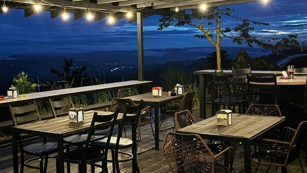 Een terras met tafels en stoelen, lichtjes en uitzicht op het landschap.