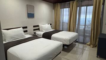 A hotel room with two beds, a large window with curtains, a ceiling fan, and a wall-mounted artwork.
