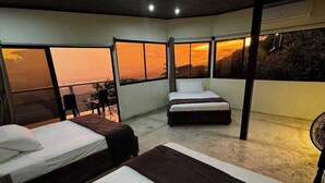 Een hotelkamer met twee bedden, een balkon en uitzicht op de ondergaande zon.