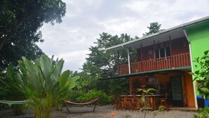 Un edifici verd amb un balcó, envoltat de plantes tropicals i una cadira espanyola.