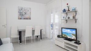 Uma sala de estar moderna com área de jantar, móveis brancos, televisão de tela plana e objetos decorativos nas prateleiras.