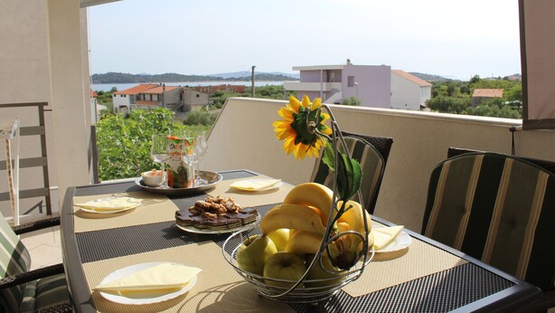 Uma mesa posta com uma cesta de frutas, um prato de comida e um vaso com um girassol.