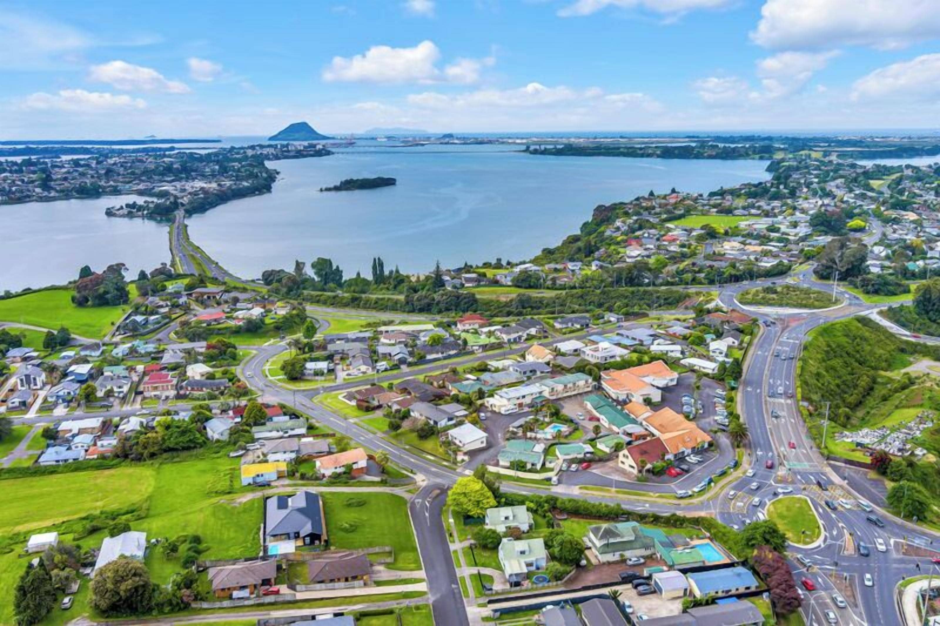 An aerial view of a coastal town with a marina, residential areas, and a prominent hill in the background.