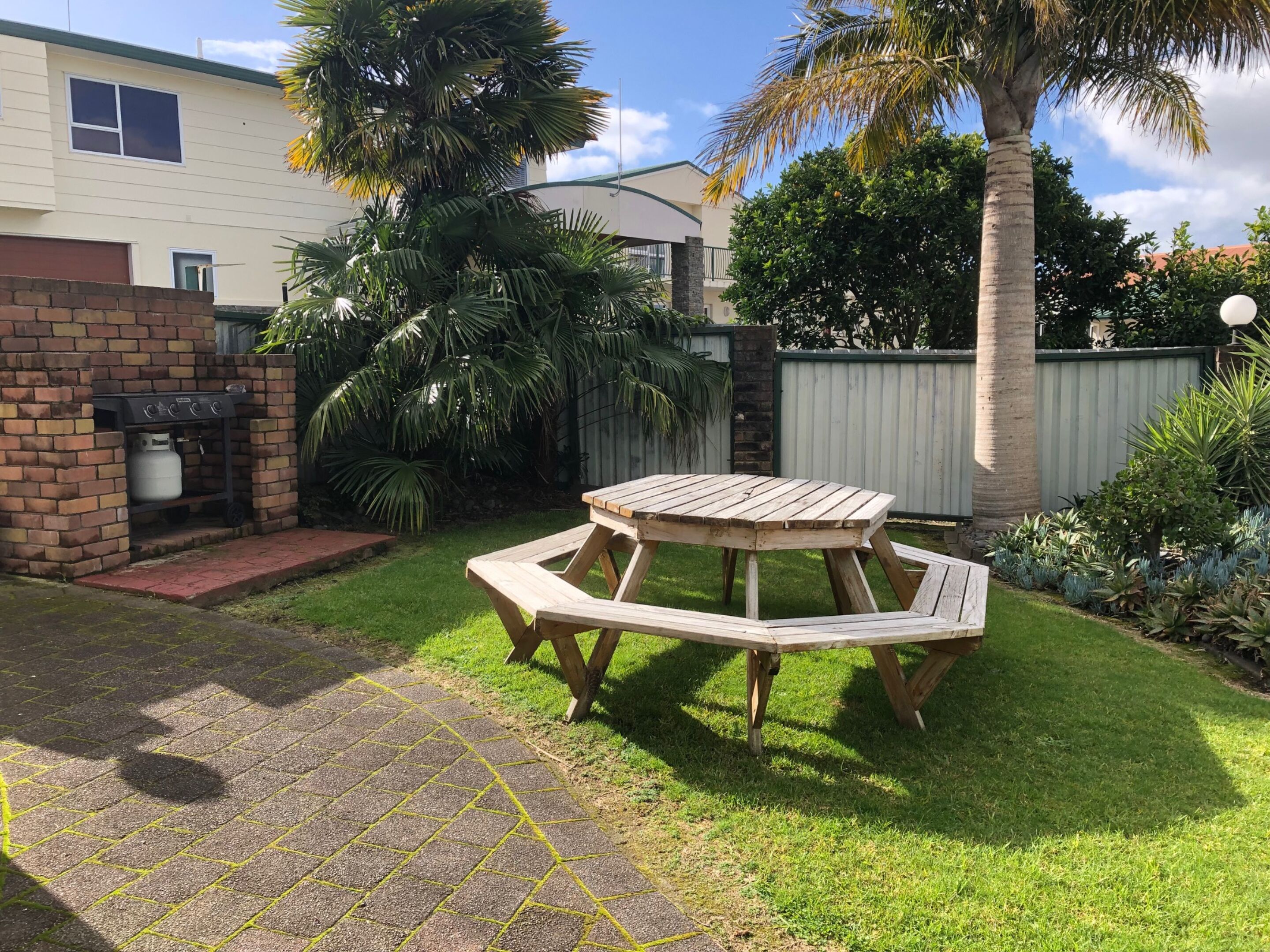 Un jardin avec une table de pique-nique en bois, un barbecue et un mur en briques.